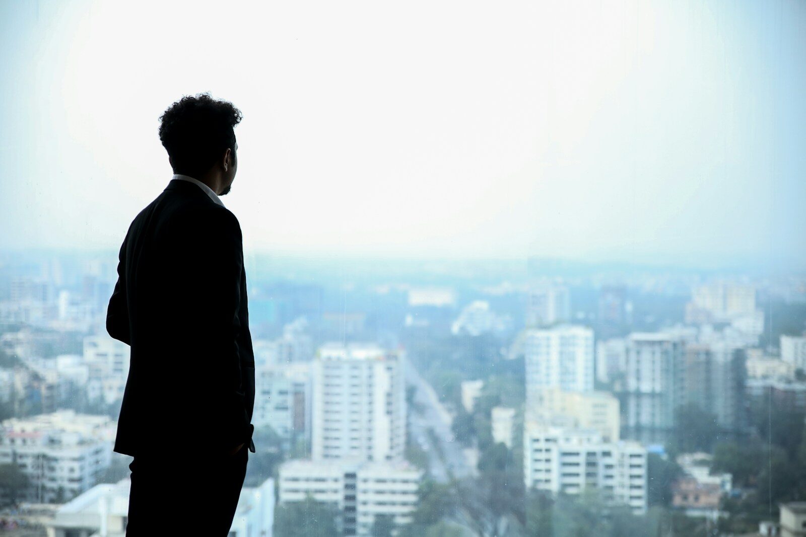 man ready to be a whistleblower in black suit standing on top of building looking at city buildings during daytime